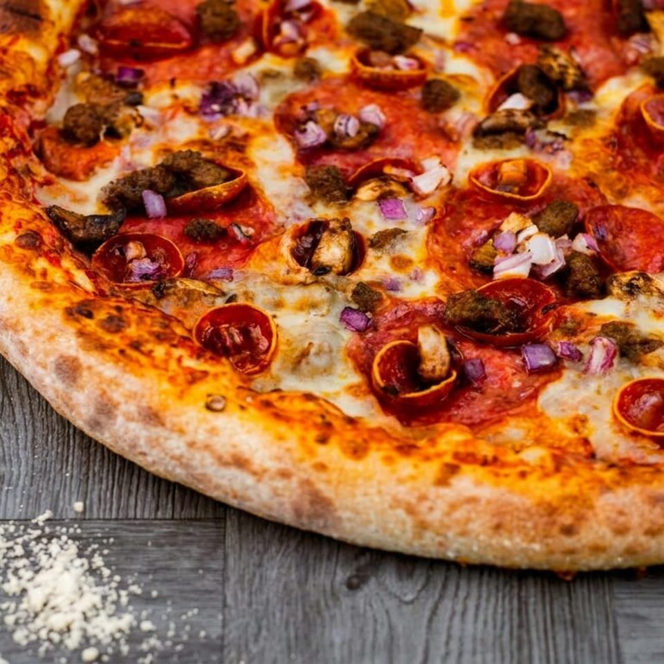 Close-up of a generously topped pizza with pepperoni, mushrooms, red onion, and browned sausage on a dark wooden table.
