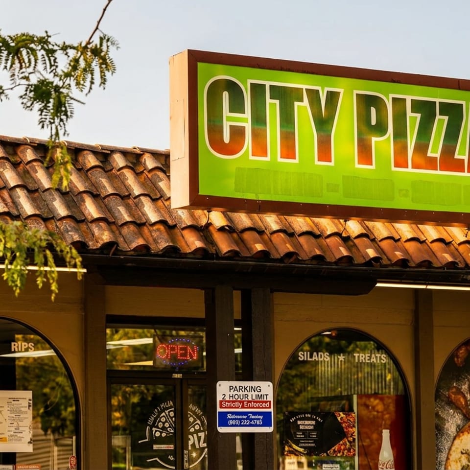 City Pizza restaurant storefront with a bright green sign, terracotta roof, arched windows, and an illuminated open sign.